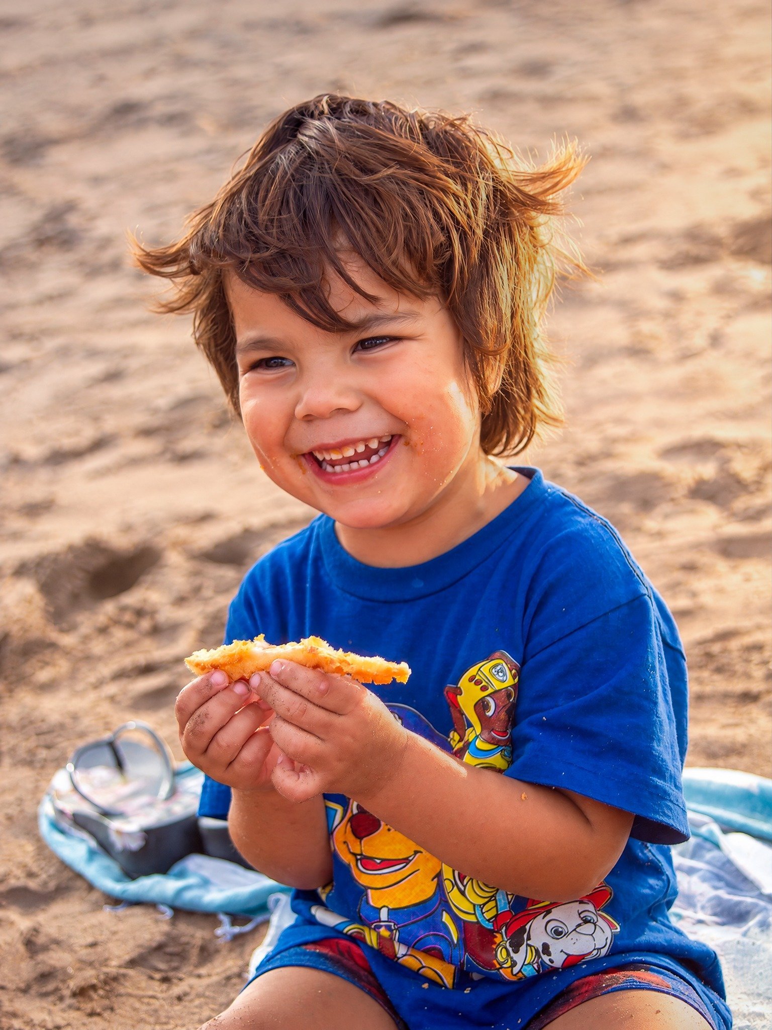 Un niño sonriente, con una remera azul, comiendo en la playa